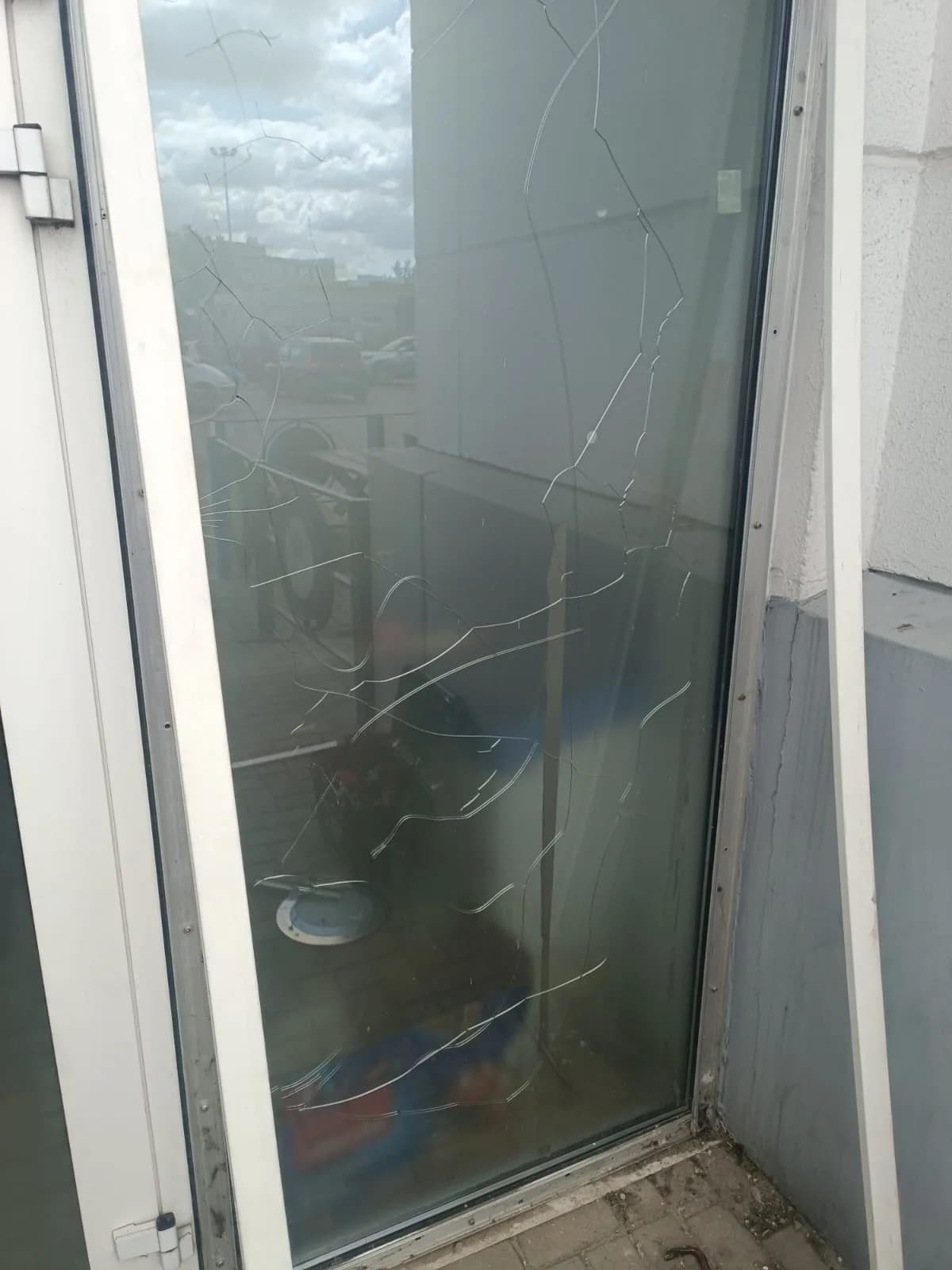 Pęknięta szyba w witrynie sklepowej, z siatką pęknięć na całej tafli przed wymianą szkła.