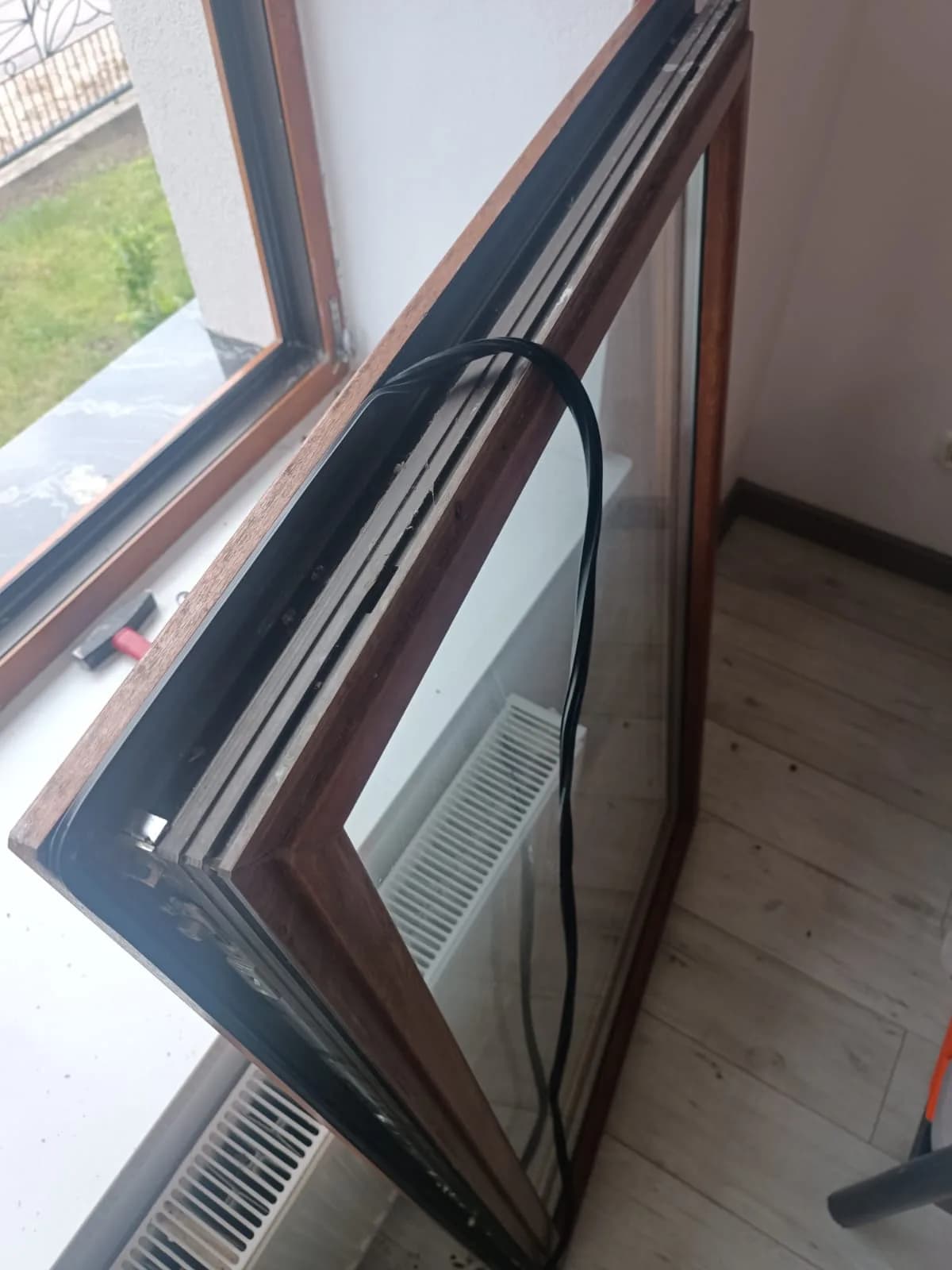 Zdjęte skrzydło okna drewnianego oparte przy oknie, widoczny rowek w ramie skrzydła po wyjęciu starej uszczelki.