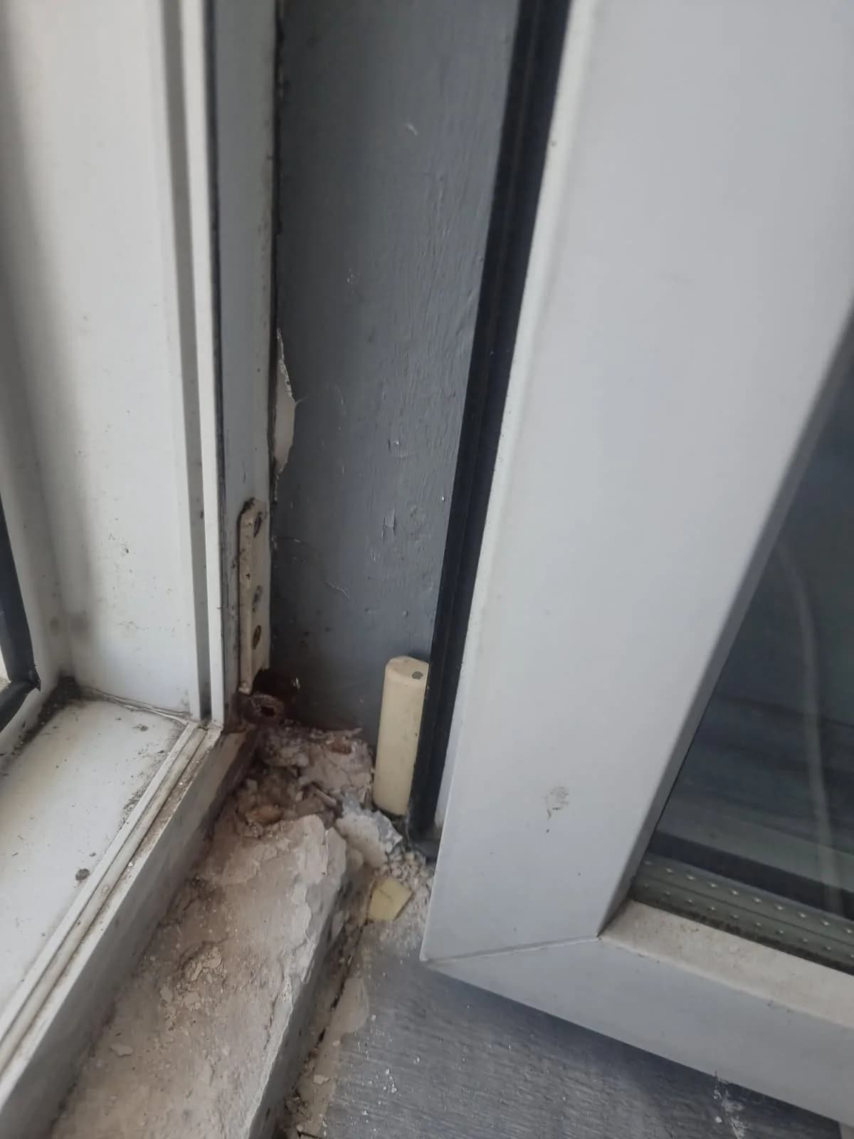 Zniszczony dolny narożnik ramy okiennej i skruszony tynk - stan przed naprawą.