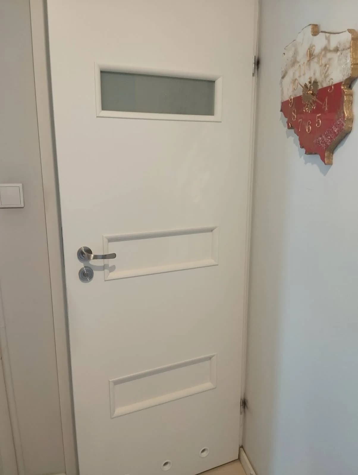 Białe drzwi wewnętrzne z przeszkleniem i panelami po regulacji zawiasów.