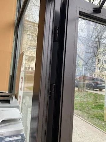 Otwarte brązowe drzwi aluminiowe w przeszklonej witrynie przed regulacją skrzydła.