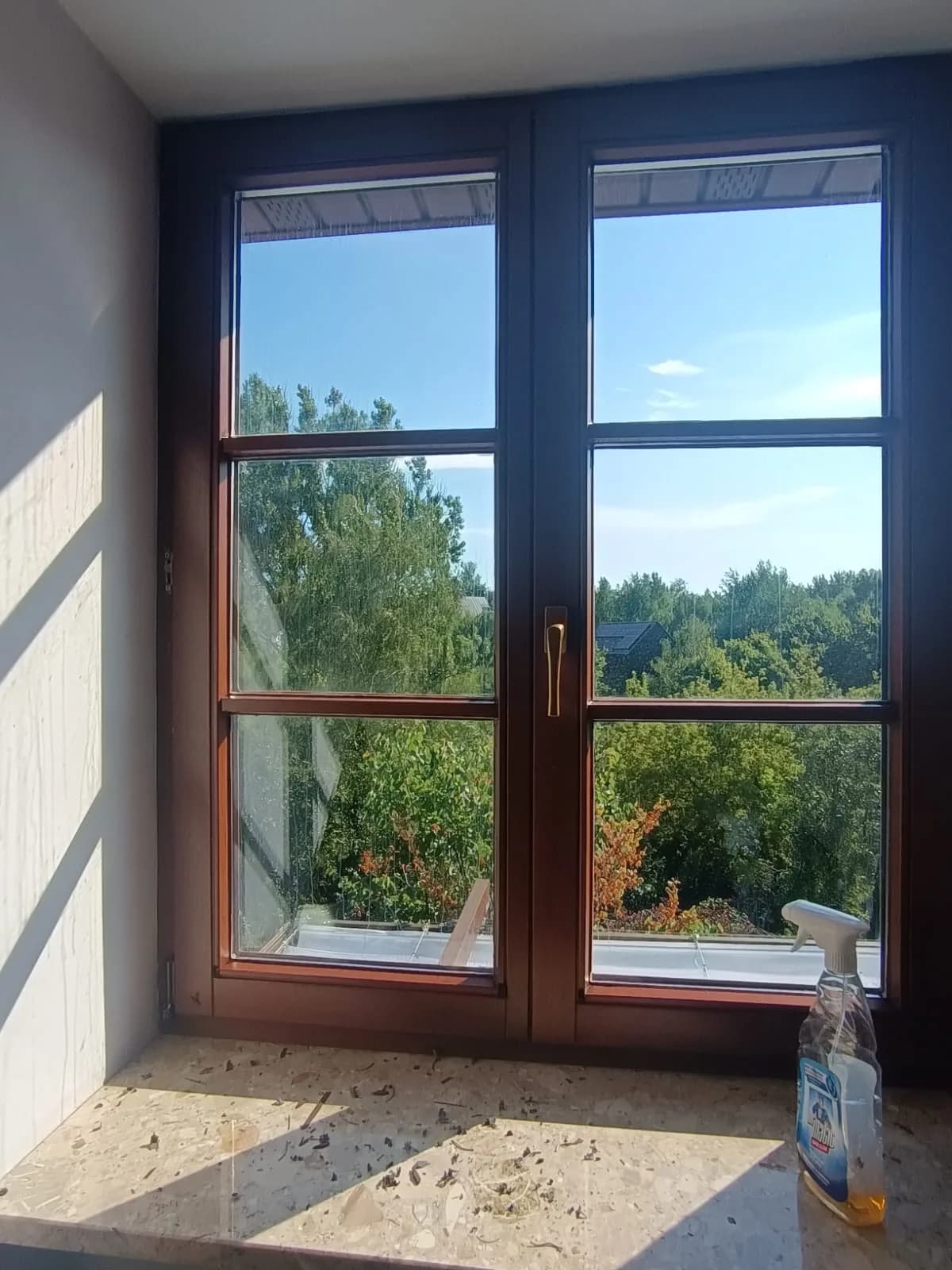 Drewniane okno ze szprosami po zakończonym serwisie, obok płyn do czyszczenia ramy i szyby.