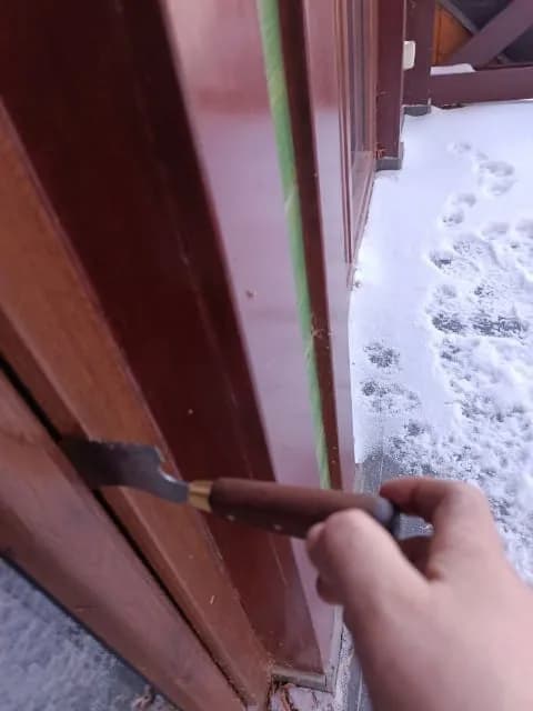 Kontrola szczelności brązowych drzwi balkonowych od strony tarasu, na zewnątrz zalega śnieg.
