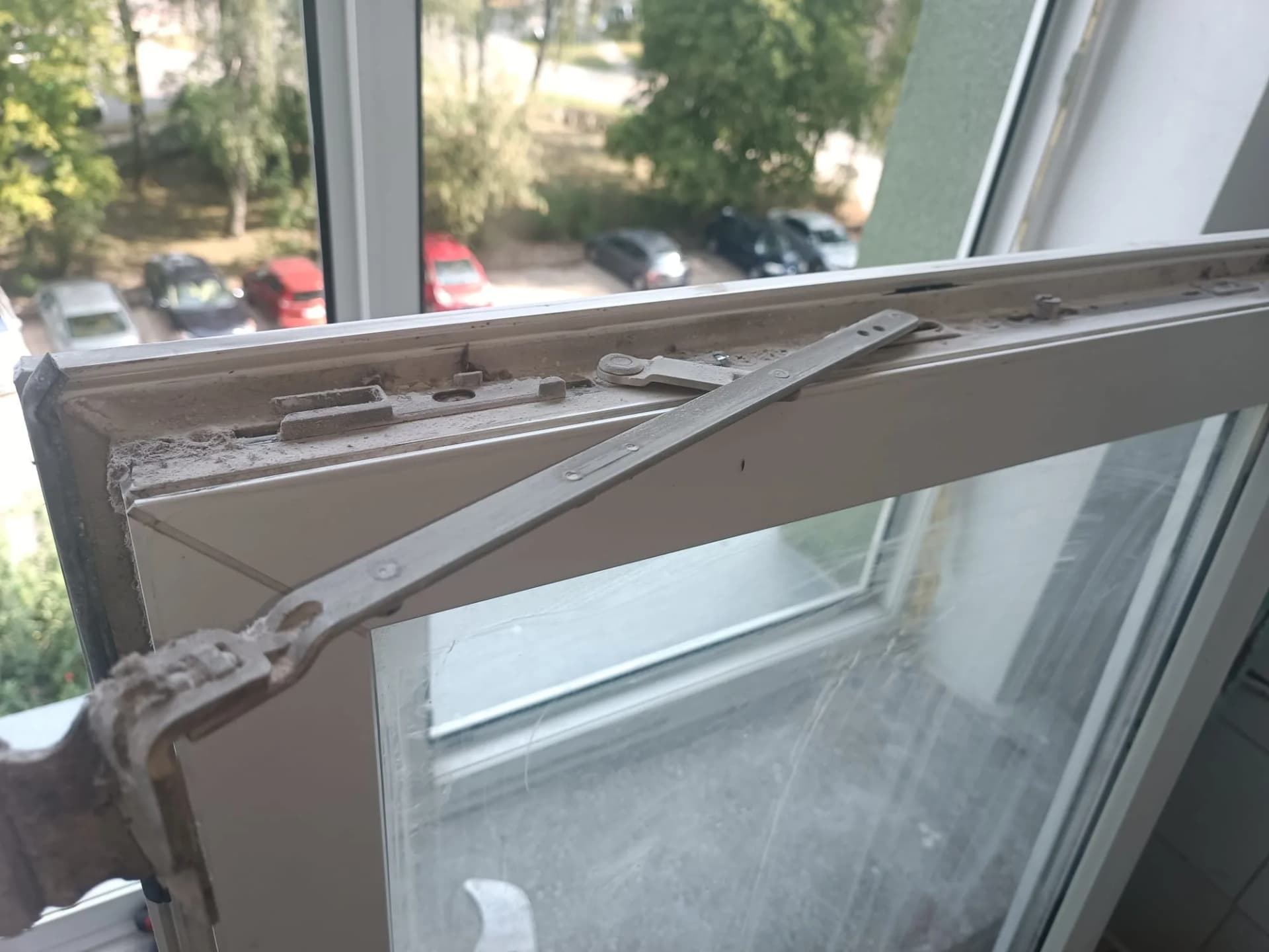 Zbliżenie górnego mechanizmu uchylnego okna PVC przed czyszczeniem i konserwacją okucia.
