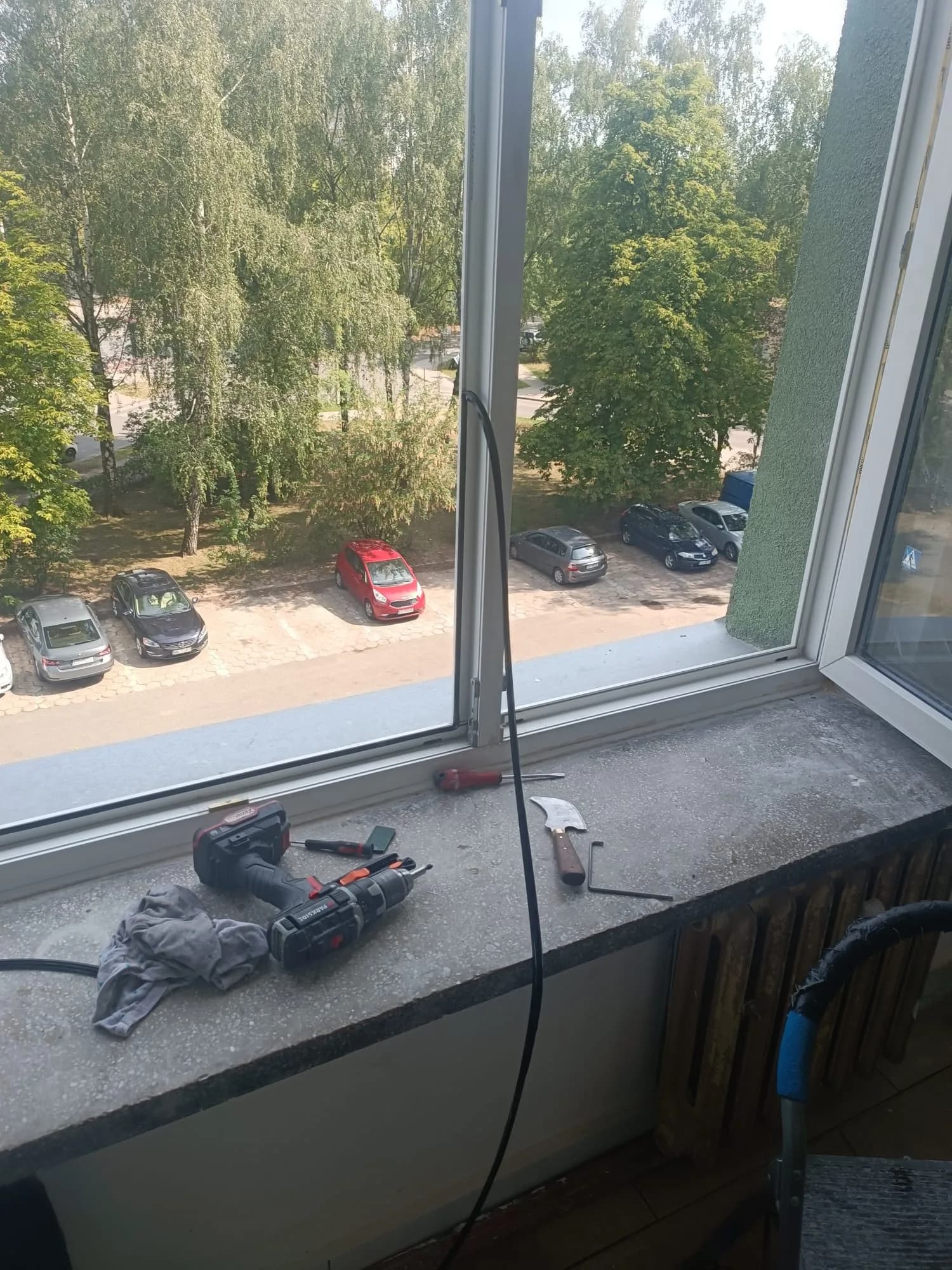 Wkrętarka, wkrętaki i klucz do regulacji ułożone na parapecie przy otwartym oknie PVC.