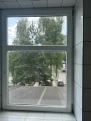 Białe okno PCV z górnym naświetlem w pomieszczeniu usługowym wyłożonym białymi płytkami.
