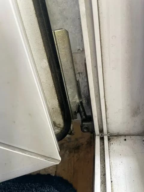 Odsłonięte okucie przy dolnym zawiasie białego okna PCV w trakcie naprawy mocowania.
