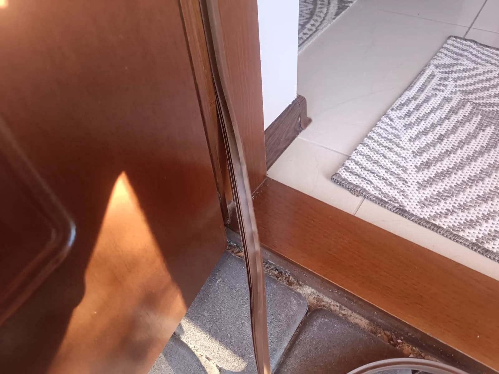Brązowa uszczelka osadzana w dolnej części drewnianych drzwi wejściowych przy progu.