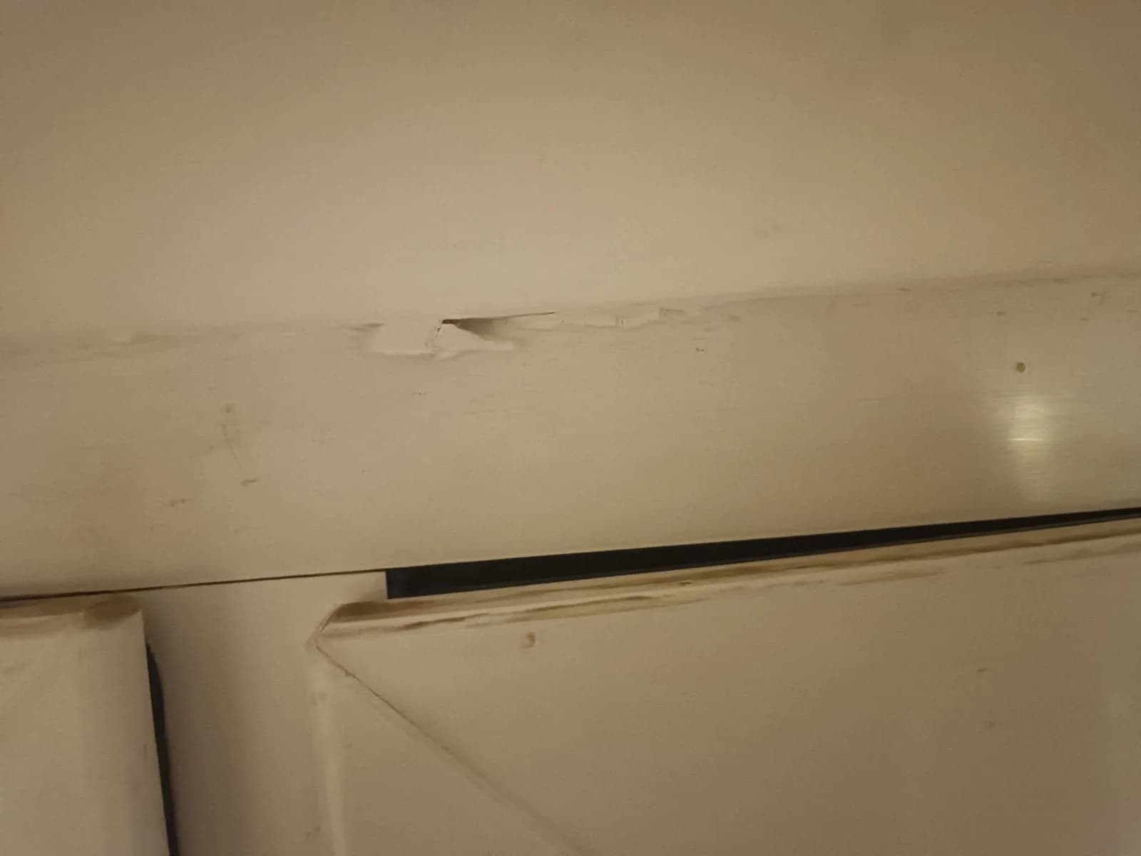 Otarcie i naderwany materiał na ramie białego okna PCV w miejscu tarcia skrzydła.