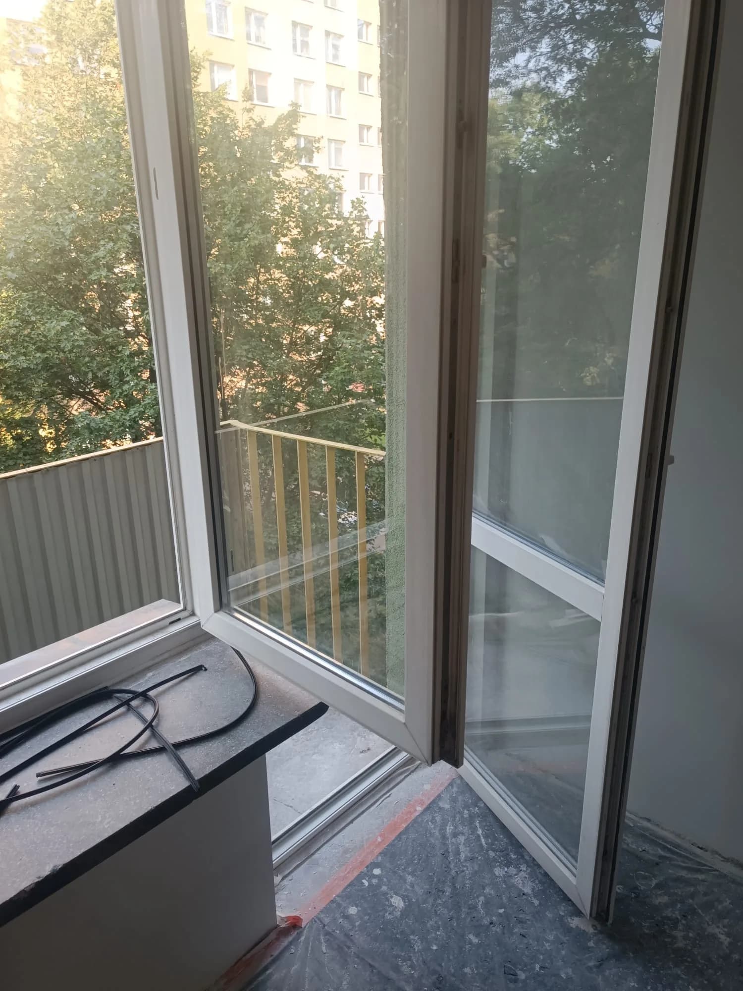 Otwarte skrzydło białego okna PVC podczas wymiany uszczelek, na parapecie zdemontowane odcinki gumy.