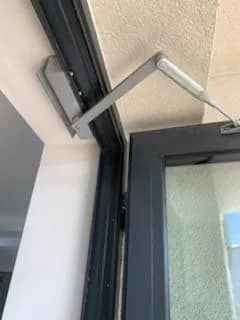 Ramię samozamykacza zamocowane nad skrzydłem antracytowych drzwi aluminiowych.