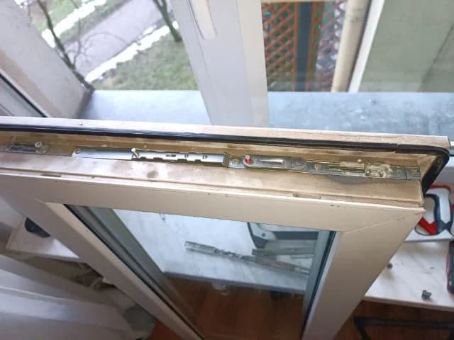 Odsłonięta rozwórka i okucie w górnej krawędzi skrzydła okna zdjętego do naprawy.