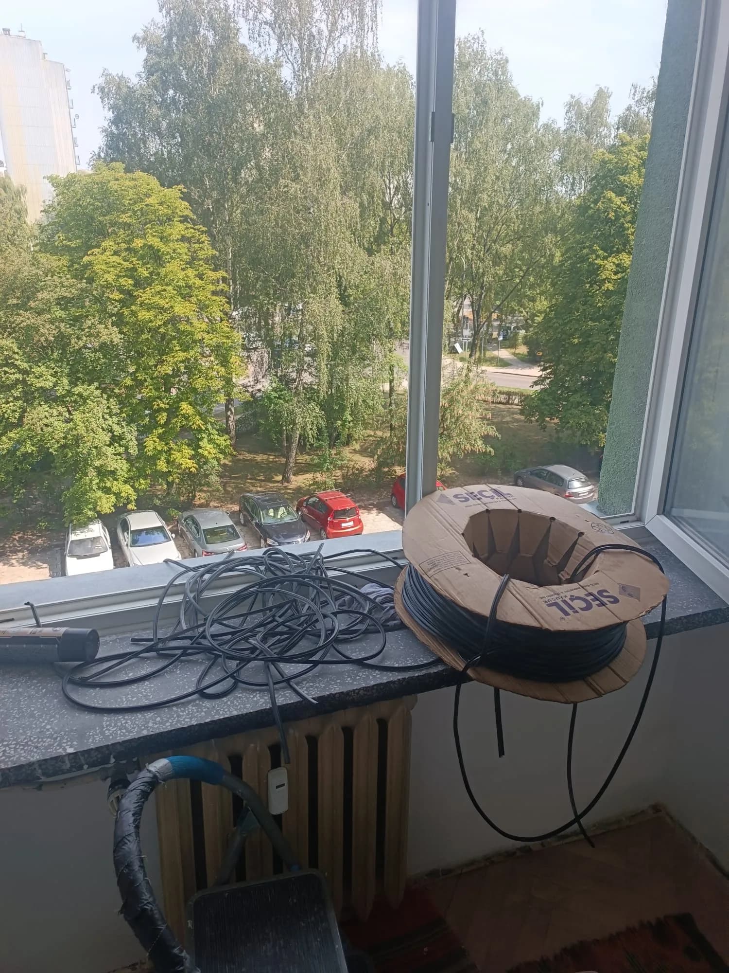 Otwarte białe okna PVC i drzwi balkonowe podczas serwisu w mieszkaniu, na parapecie usunięte uszczelki.
