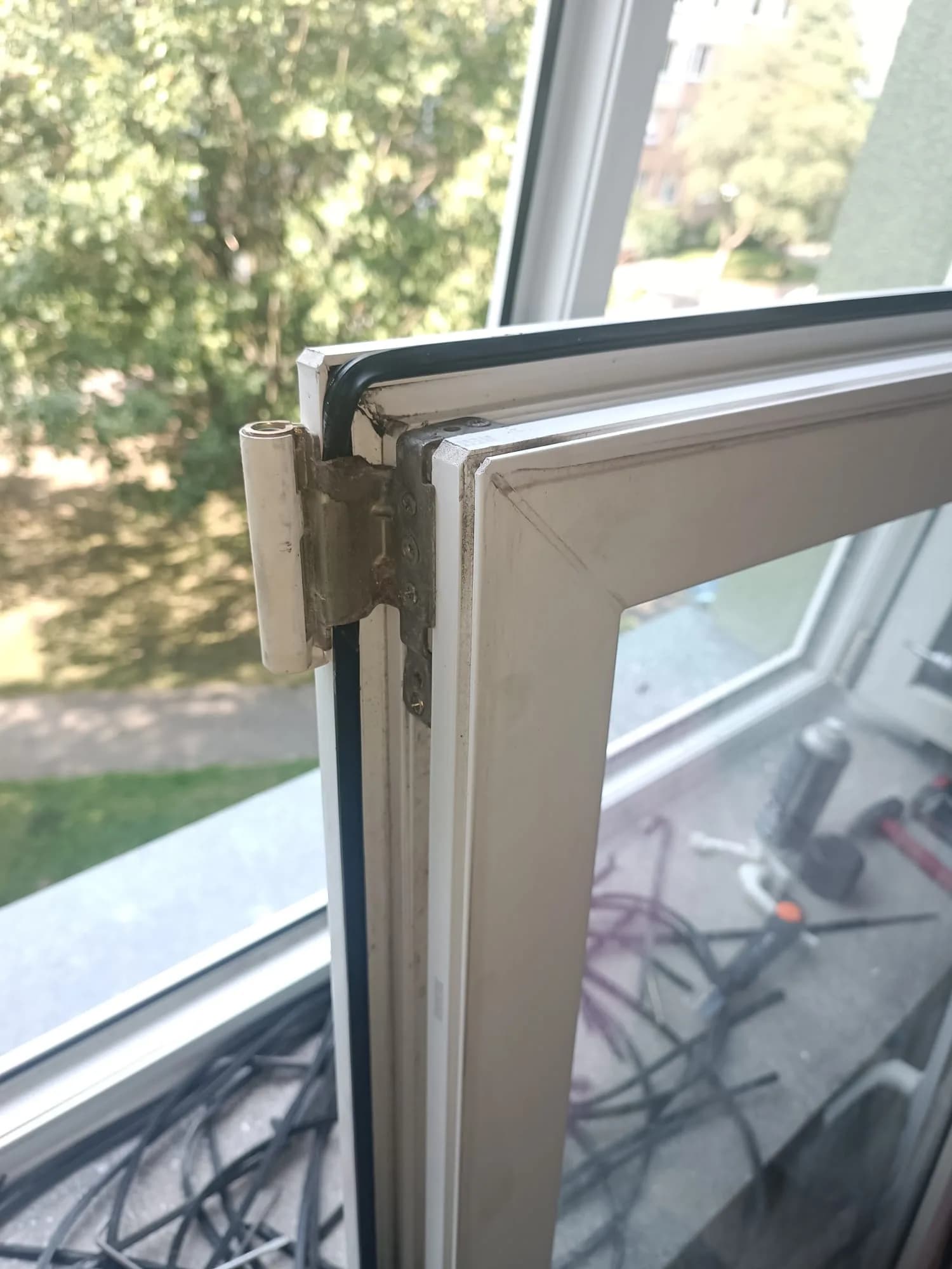 Otwarte białe okno PVC podczas serwisu, na parapecie uszczelki, wkrętarka i narzędzia.