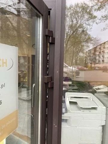 Skrzydło brązowych drzwi aluminiowych z dwoma zawiasami w przeszklonej witrynie biurowej.