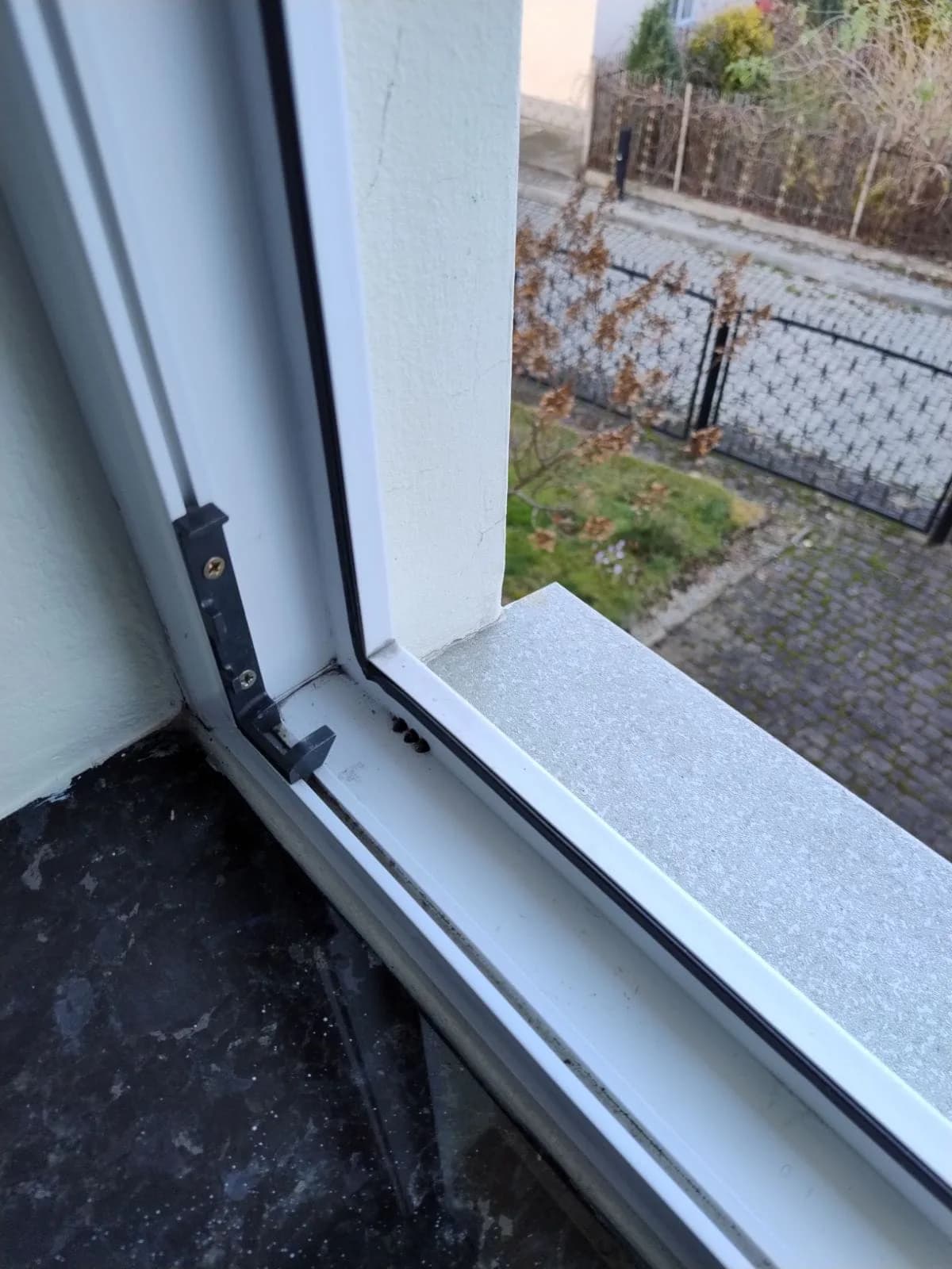 Stara czarna uszczelka i zawias w narożniku białego okna PCV przed wymianą.