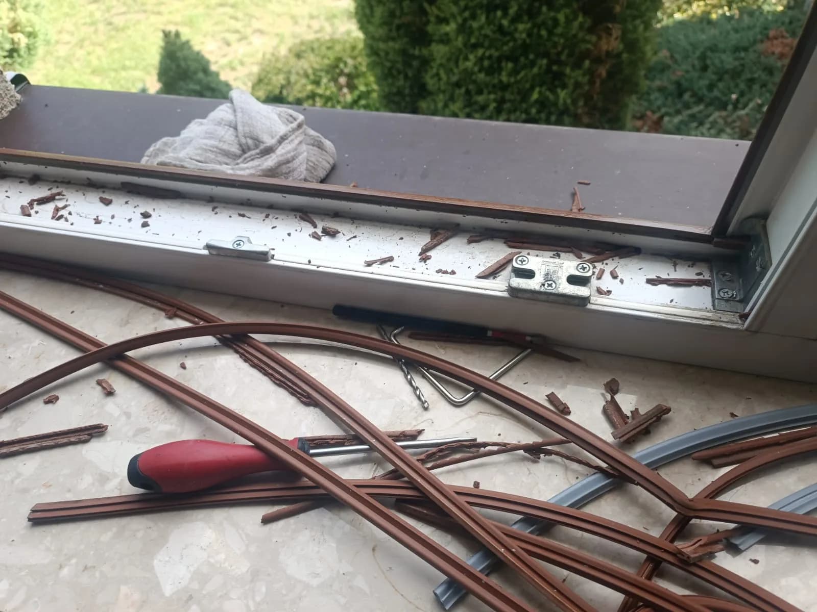 Stare brązowe i nowe szare uszczelki oraz narzędzia ułożone przy otwartym oknie podczas wymiany.