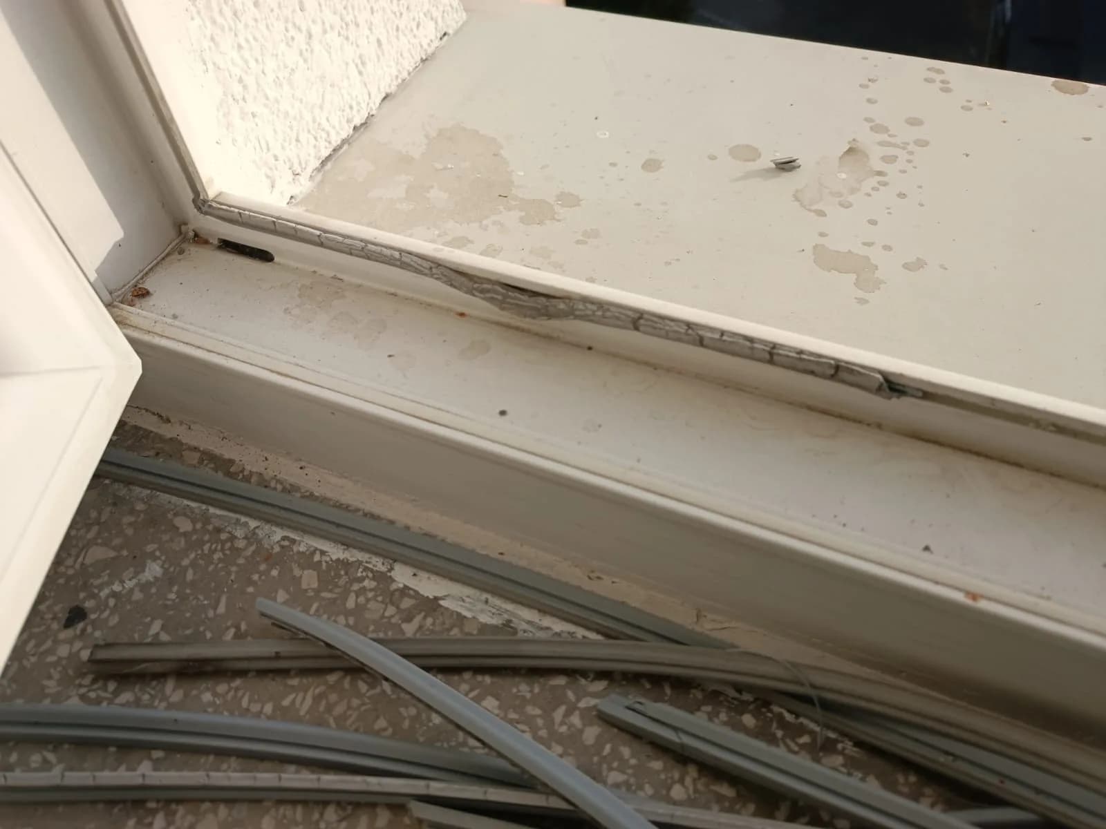 Zdjęte stare uszczelki na parapecie i zabrudzona rama okna przed oczyszczeniem rowka.