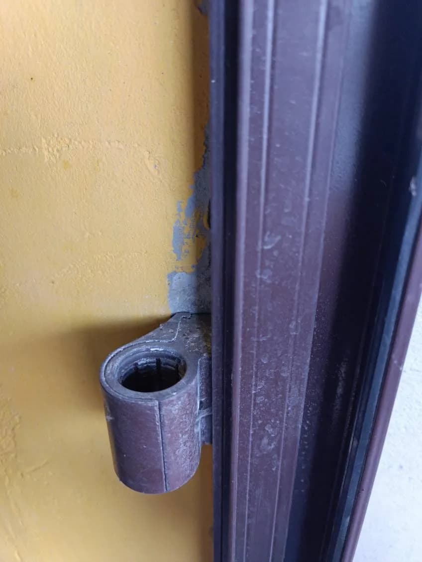 Tuleja dolnego zawiasu brązowych drzwi aluminiowych osadzona przy ościeżnicy.