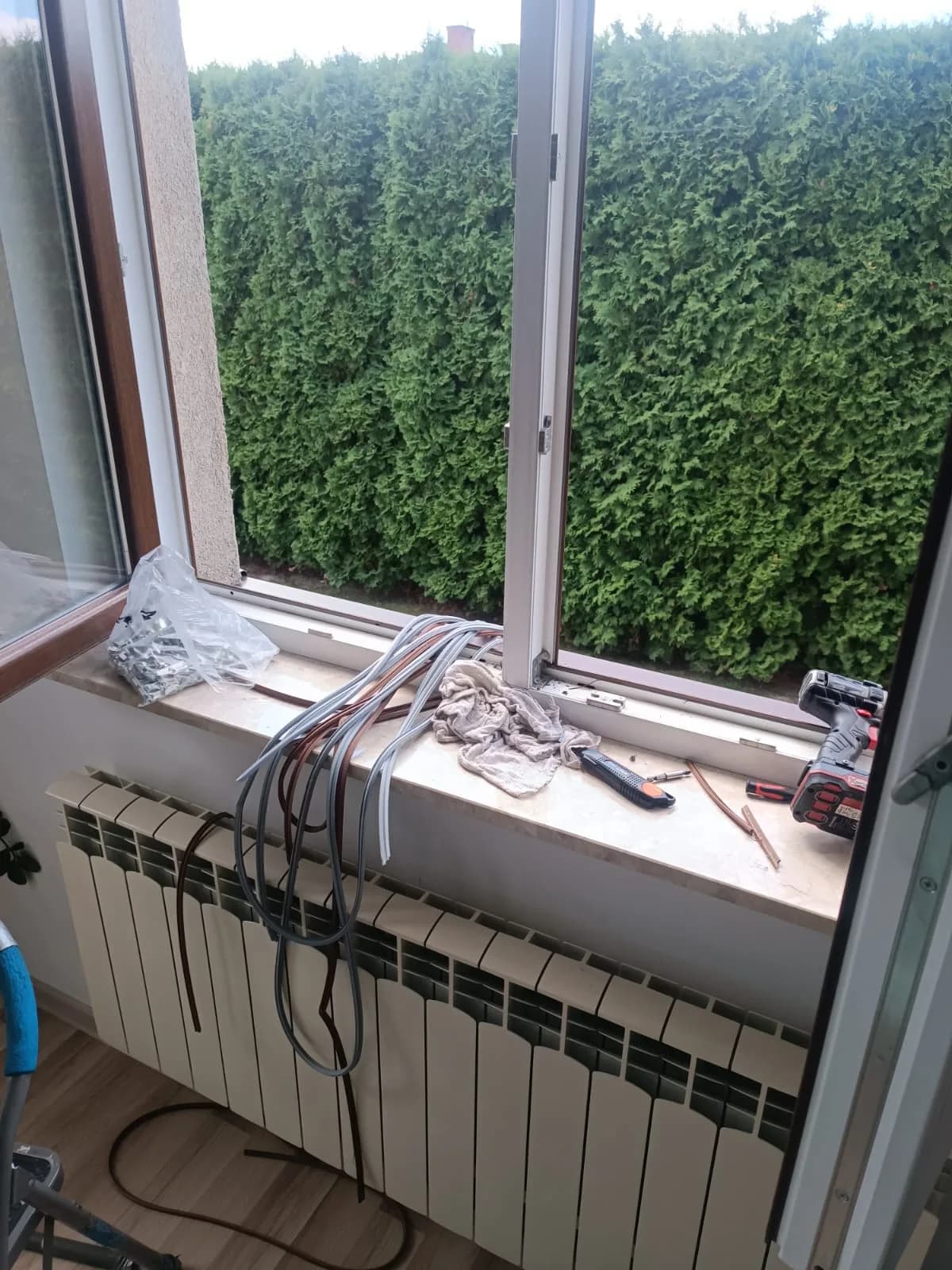 Szare i brązowe uszczelki, wkrętarka oraz nóż ułożone na parapecie otwartego okna podczas wymiany.