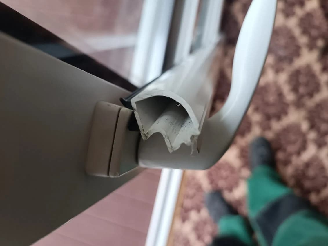 Naderwana listwa PCV przy krawędzi kremowego skrzydła okiennego przed wymianą.