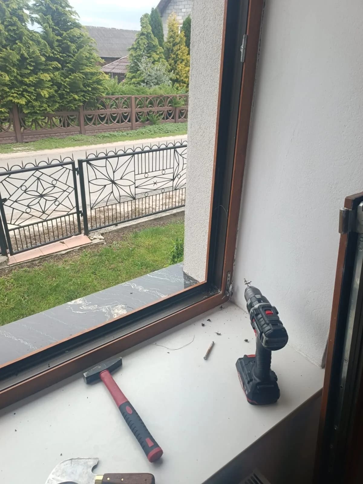 Narożnik ramy okna drewnianego przy okuciu, na parapecie wkrętarka, młotek i wykręcony wkręt.