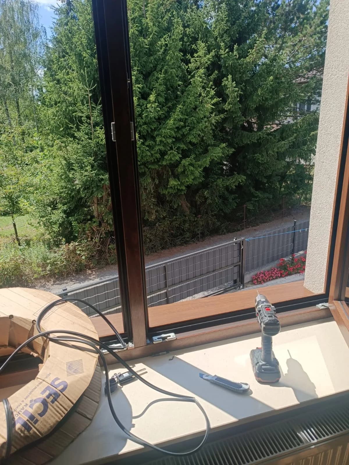 Szpula czarnej uszczelki, wkrętarka i nóż na parapecie drewnianego okna podczas wymiany uszczelek.
