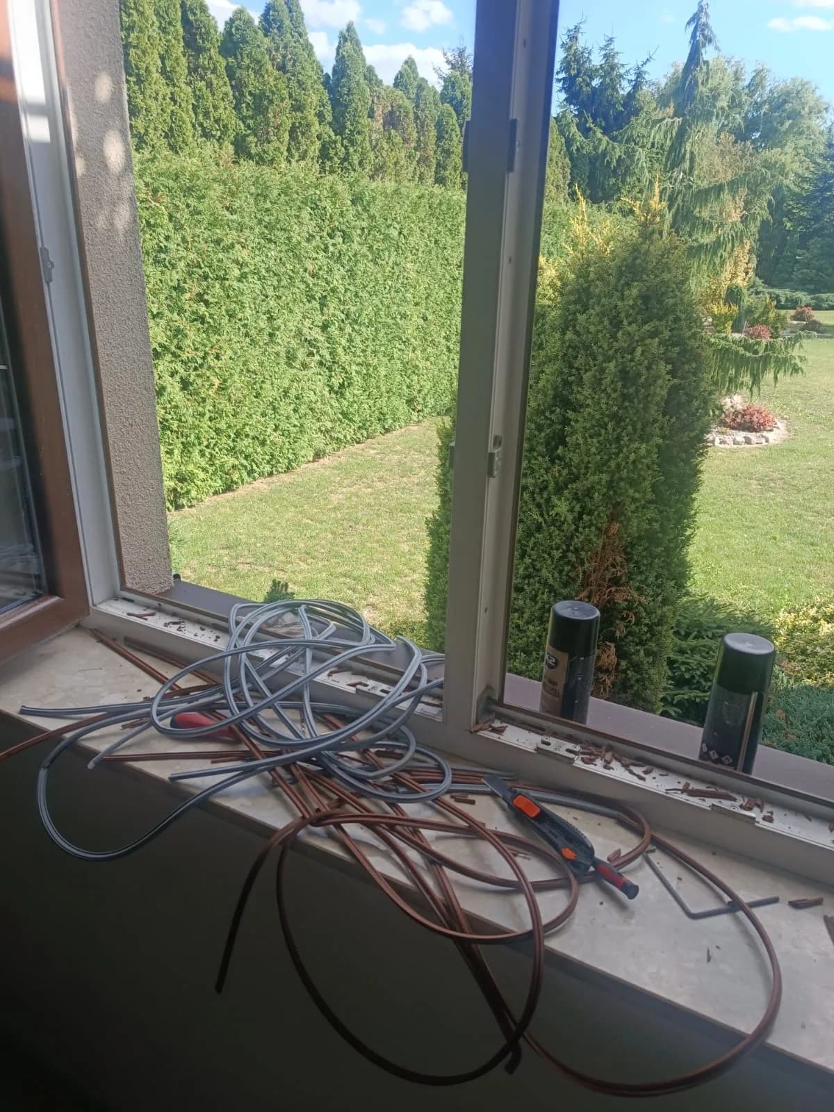 Otwarte okno z przygotowanymi szarymi i brązowymi uszczelkami oraz narzędziami na parapecie.