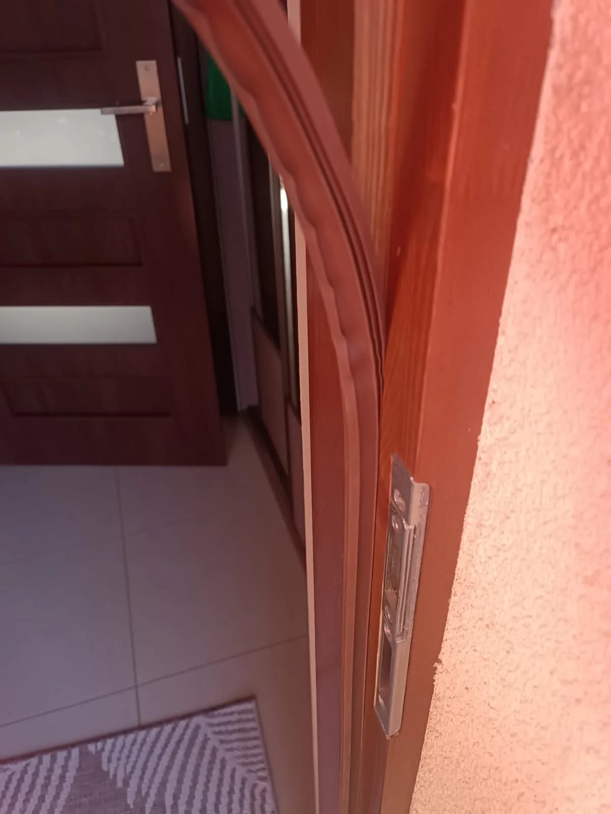 Metalowy zaczep zamka osadzony w ościeżnicy drewnianych drzwi wejściowych.