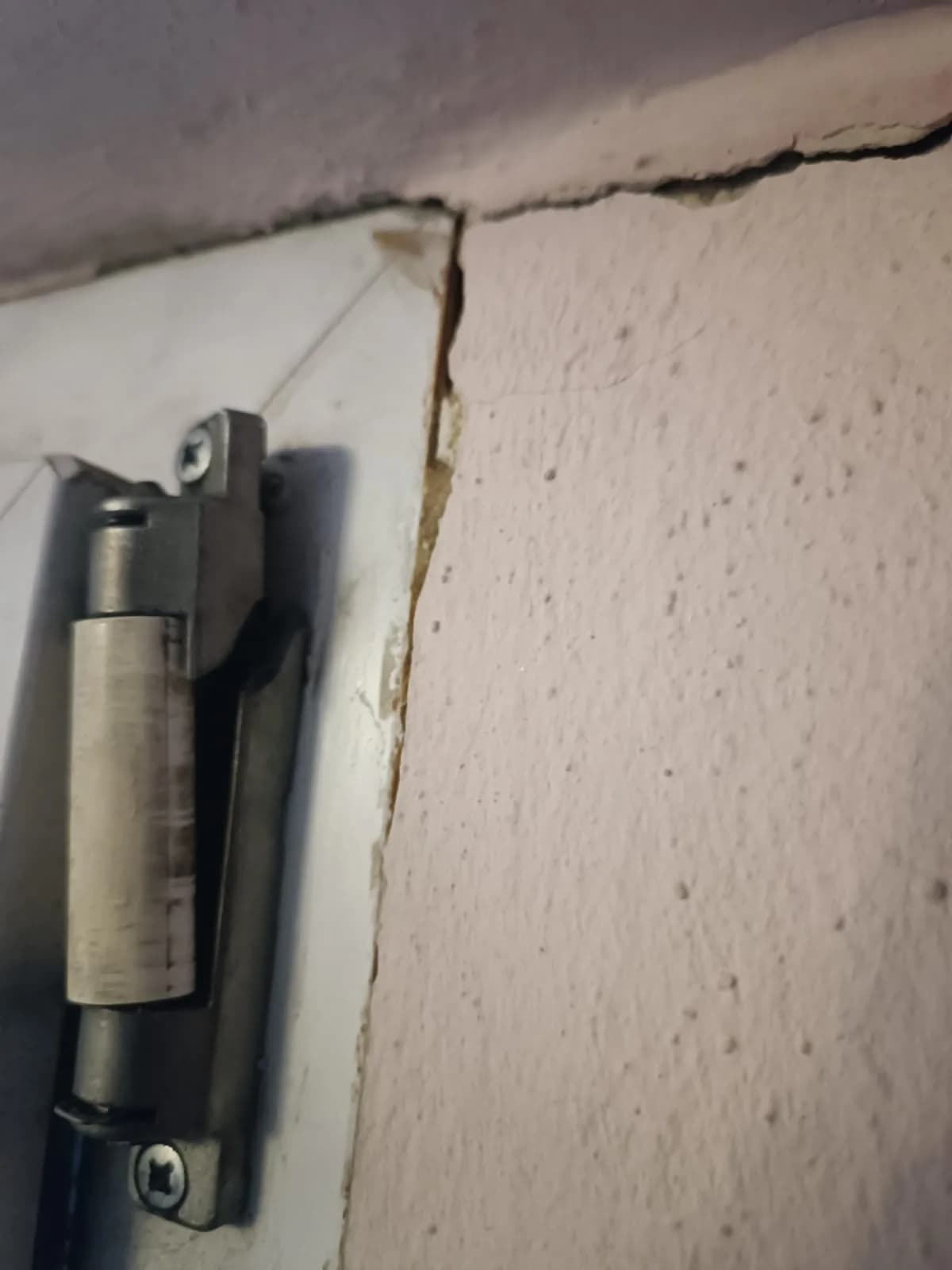 Metalowy zaczep zamka w ościeżnicy drzwi oraz pęknięty tynk nad nim przed naprawą.