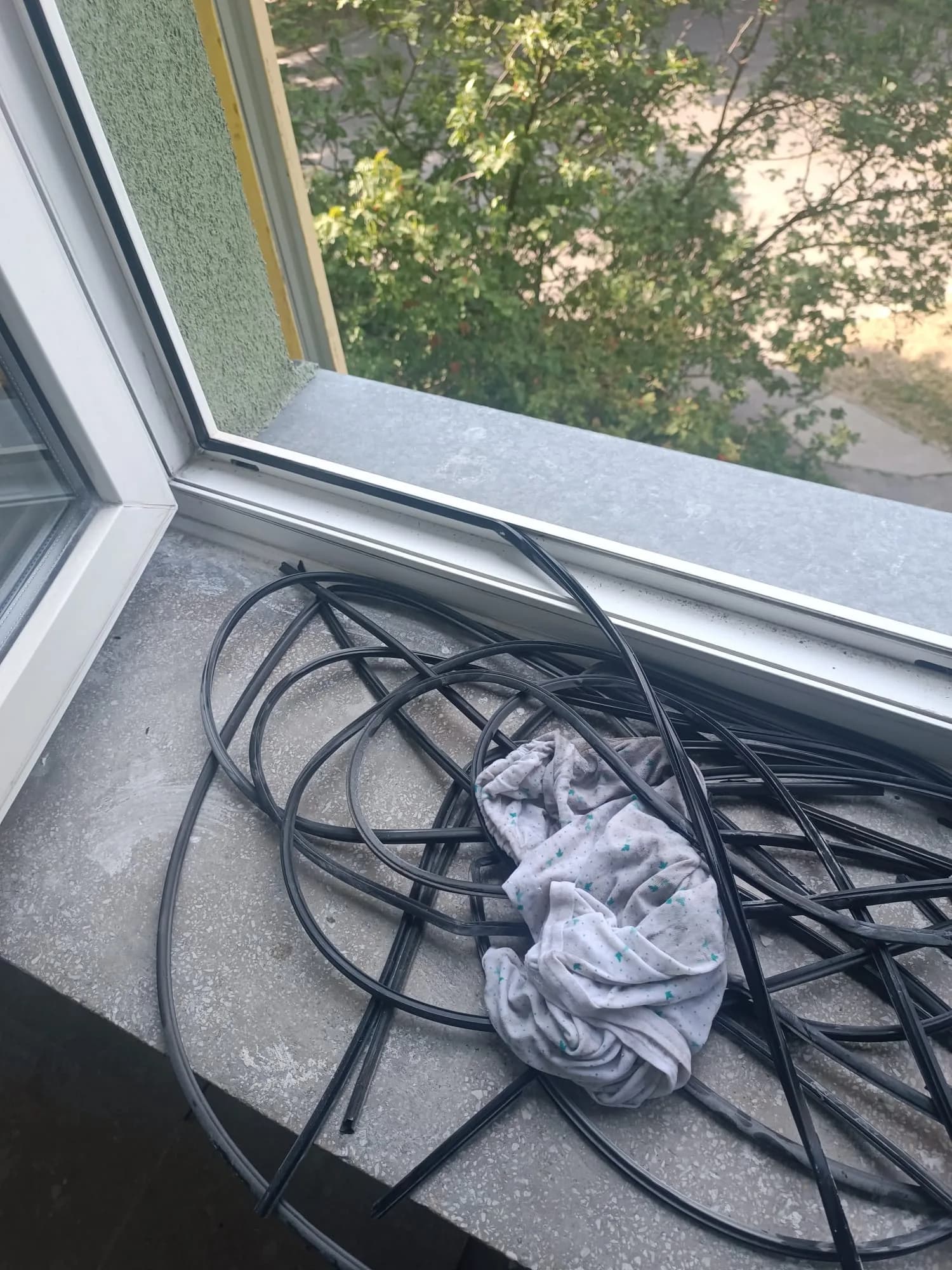 Zdemontowane czarne uszczelki z okna PVC ułożone na parapecie obok ściereczki.