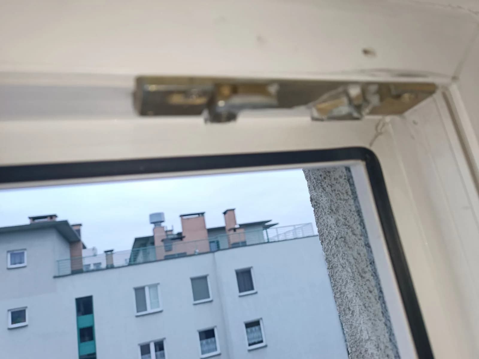 Odsłonięte okucie Roto w górnym narożniku okna PCV podczas czyszczenia i smarowania.